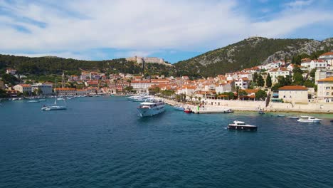 -Panorama-of-a-coastal-town-with-many-houses-with-red-roofs,-surrounded-by-the-sea-and-mountains-with-yachts-in-marina-bay-and-Bell-tower