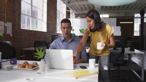 Diverse-male-and-female-business-colleagues-in-discussion-at-work-using-laptop