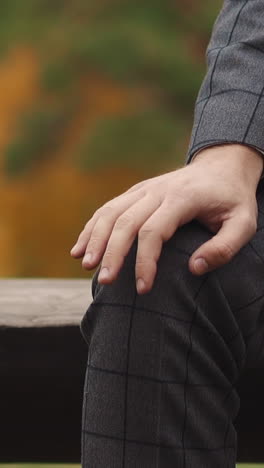 guy in checkered office suit taps fingers on knee sitting on wooden bench on city street close view slow motion. manager waiting at stress situation