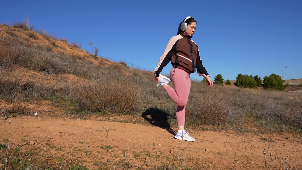 mujer corriendo cuesta abajo se detiene para estirar sus cuádriceps y pantorrillas