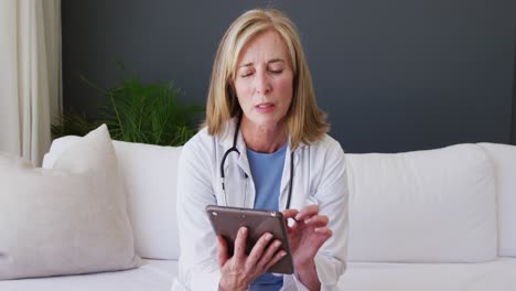 portrait of caucasian senior female doctor using digital tablet while having a video call at home