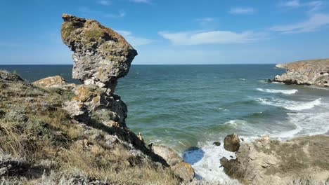 Waves-crash-against-the-rocky-shoreline-as-the-unique-natural-formations-of-Crimea-stand-against-a-clear-blue-sky