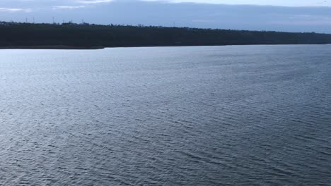 Side-tracking-shot-over-a-big-lake-on-a-windy-cold-day,-drone-shot,-light-reflections