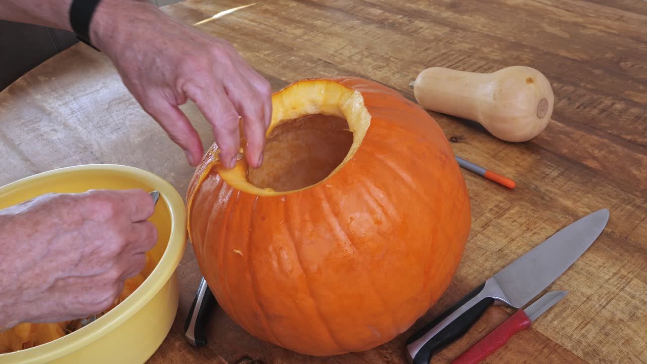 Scooping raw pumpkin seeds and pulp into bowl for Halloween preparation
