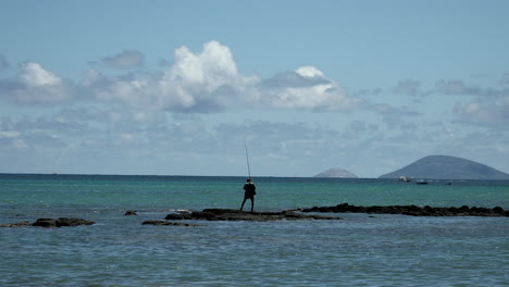 fisherman standing on rock in ocean and angling fish with rud