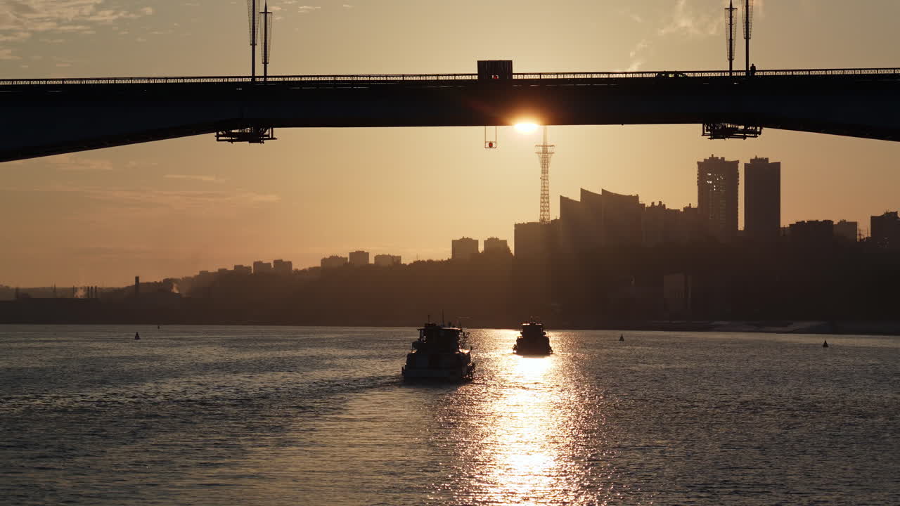 Sunset over a city river with boats and a bridge silhouette