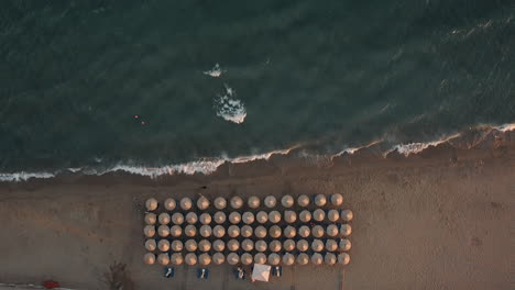 Flying-over-seaside-with-chaise-longues-under-straw-umbrellas