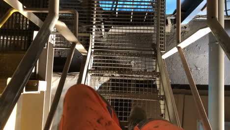 foto de un trabajador con los pies mientras baja las escaleras en una fábrica, usando ropa de seguridad naranja muy visible