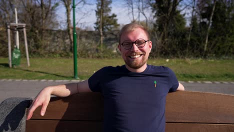 caucasian man sitting on outdoor bench and laughs, medium parallax shot