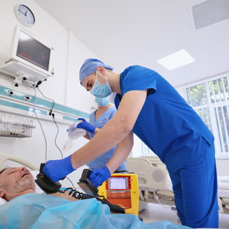 male surgeon resuscitating an unconscious patient with a defibrillator in hospital. nurse and male doctor in medical uniform help the patient in reanimation room.