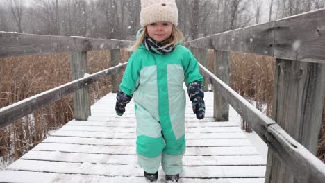 little girl running on nature boardwalk in winter slow motion snow falling