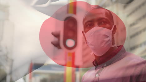 animation of flag of japan waving over man wearing face mask during covid 19 pandemic