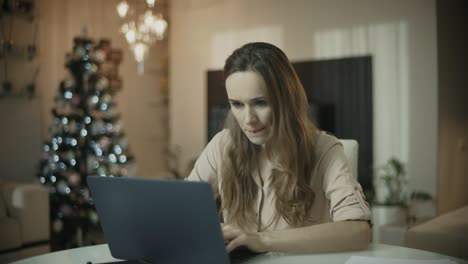 Young-woman-working-on-laptop-computer-at-christmas-home