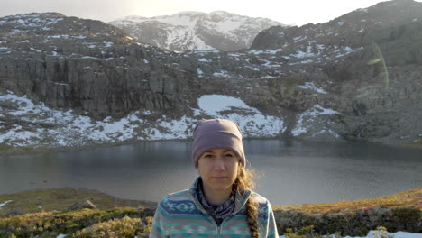 a woman looks towards the camera with a calm expression while on a sunset hike on a mountain in norway, static slow motion