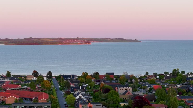 Vista aerea di una città costiera al tramonto ripresa da un drone, con case colorate in primo piano e le acque calme dell'oceano che si estendono fino alla costa in lontananza