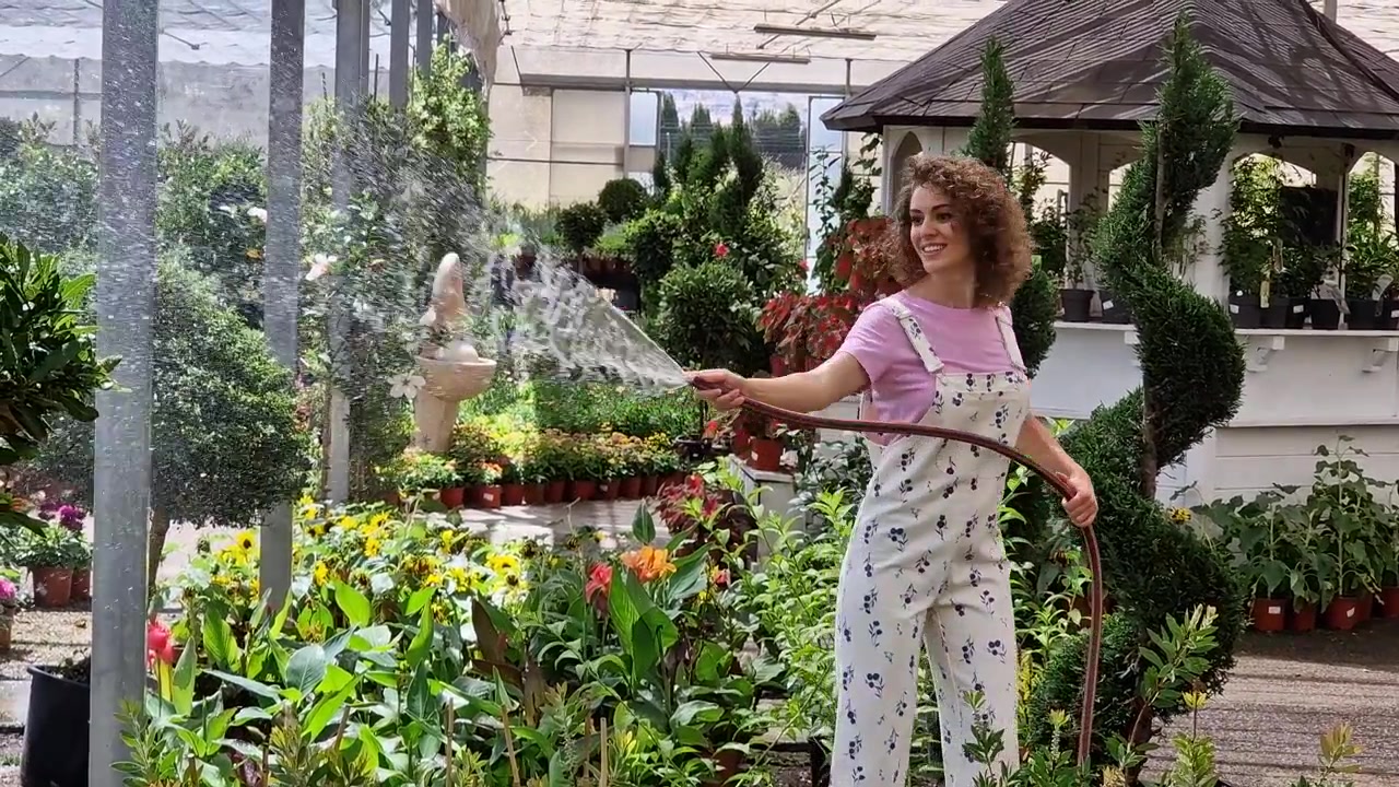 Молодая кудрявая женщина-садовод поливает цветущие растения.