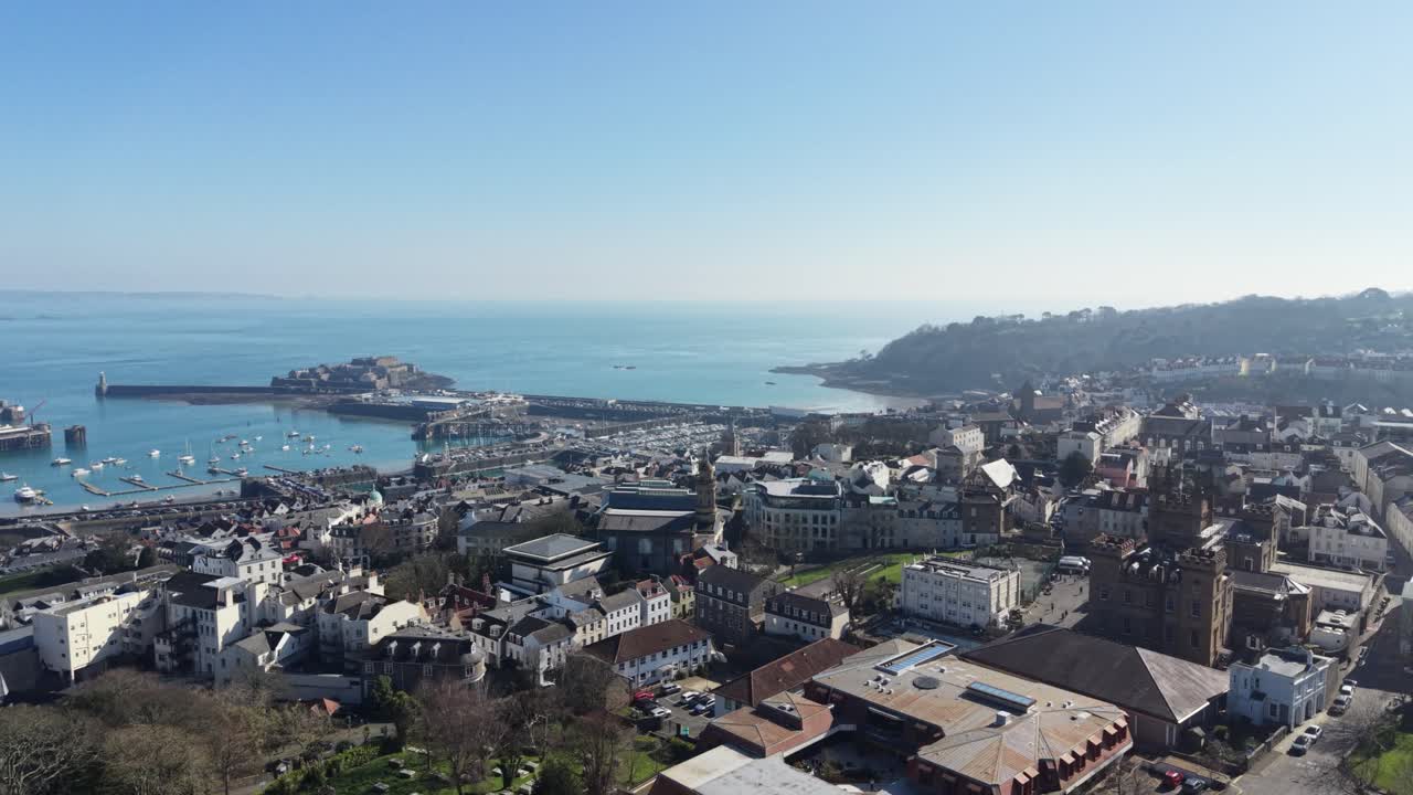 St Peter Port Guernsey, riprese aeree ad alta quota della sala dell'Assemblea di St James e dell'Elizabeth College con viste sulla città, sul porto, sul Castello Cornet, sulla Baia di Havelet verso Herm, Jethou e Sark sotto il sole splendente.