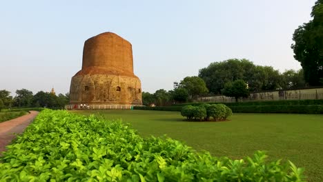 Ein-Weitläufiger-Panorama-Gleitflug-Mit-Blick-Auf-Die-Grünen-Rasenflächen-Von-Dhamek-Stupa-In-Varanasi,-Indien