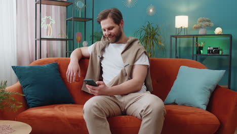 caucasian young man sitting on sofa using smartphone share messages on social media application
