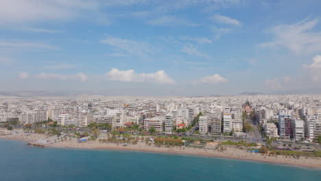 Toma-Aérea-Ascendente-Desde-El-Mar-Azul-Hasta-Los-Edificios-Blancos-De-La-Ciudad-De-Atenas,-Grecia