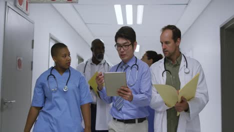 Grupo-Diverso-De-Médicos-Y-Mujeres-Hablando-En-El-Pasillo-Del-Hospital,-Caminando-Con-Tableta-Y-Archivo