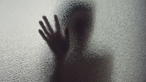 a female silhouette behind the frosted glass moves slowly