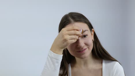 Fröhliche-Und-Umwerfend-Aussehende-Junge-Kaukasische-Frau,-Die-Vor-Einem-Weißen-Hintergrund-Mit-Einem-Pinsel-Make-up-Auf-Ihr-Gesicht-Aufträgt