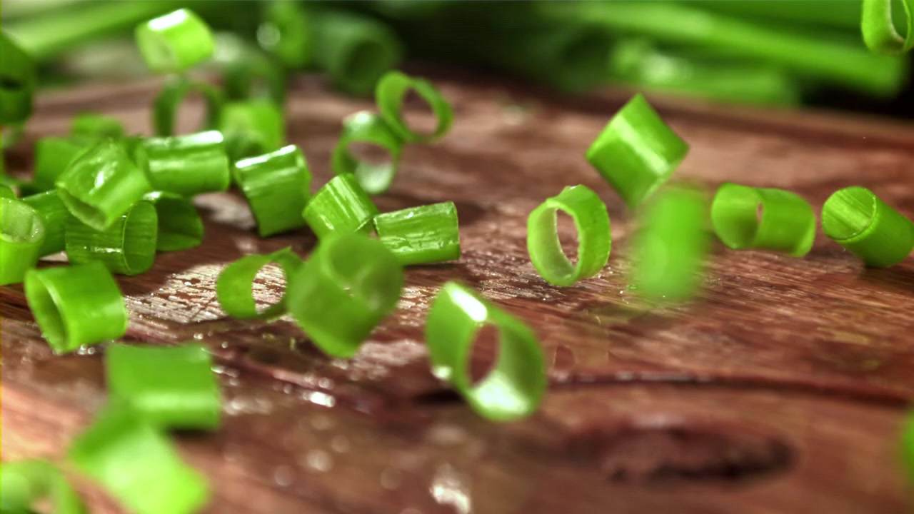 Chopped Green Onions Falling onto a Wooden Cutting Board in Slow Motion