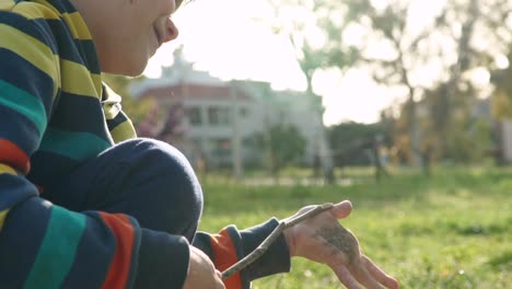 Side-view-120-fps-tight-shot-of-caucasian-kid-playing-with-dust-in-his-hands,-using-a-wooden-stick