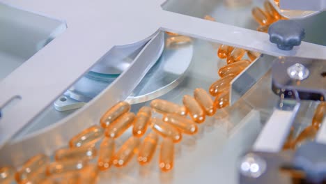 slow motion of orange gel capsules moving inside a packaging machine