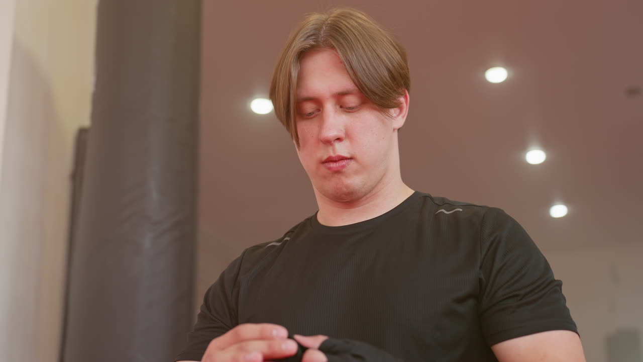 Athlete in black sportswear standing under bright ceiling lights with determined expression, preparing mentally for training session, showing focus, resilience inside professional gym environment