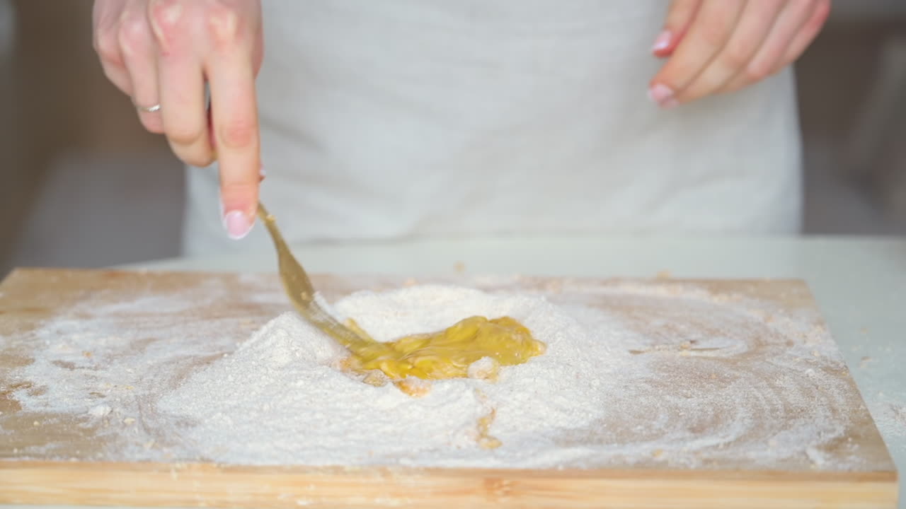 Woman wearing an apron, mixing an egg in flour on a wooden cutting board in the kitchen