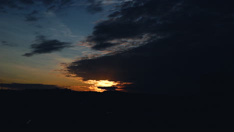 a bright blue sky with an orange sunset is covered by dark clouds, clouds move and build new layers in the sky