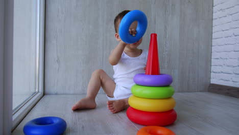 cute caucasian baby plays on the floor collecting a pyramid. happy smiling kid paying a game.