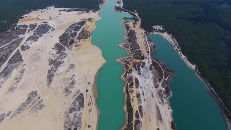 a spectacular 4k drone shot of the long and narrow crystal lake. this bright-blue colored lake is located in a sandy, desert-like titanium mine, in the pine barrens of manchester township, new jersey