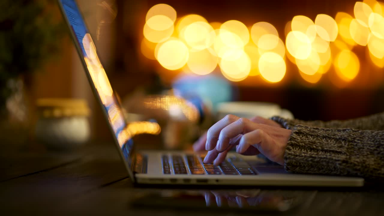 Woman wearing wool sweater typing fast with her fingers on her laptop, writing an article online and doing her job. Home celebration environment. Sliding shot, 4K