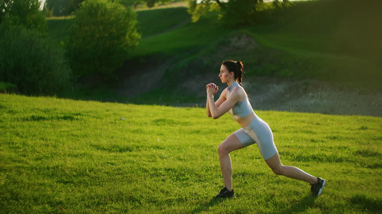 A woman in the park performs lunges on each leg in the morning. Morning training.