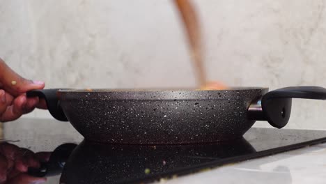 a person stirs food in a pan on a stovetop