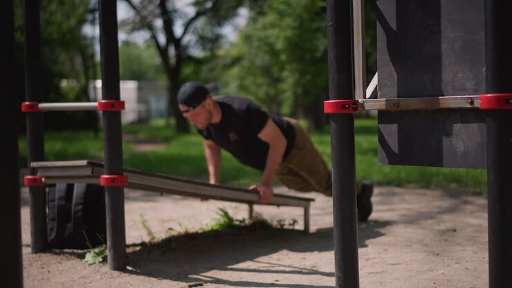 Individual Performs Controlled Pushups Outside, Male Practicing Disciplined Calisthenics Beneath Trees In Park, Person Engages In Structured Bodyweight Workout Under Shade Amidst Grassy Park Scenery