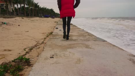 A-lady-walking-on-concrete-road-between-sand-and-sea