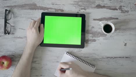 male hands make notes in a notebook, next is a tablet with a green screen