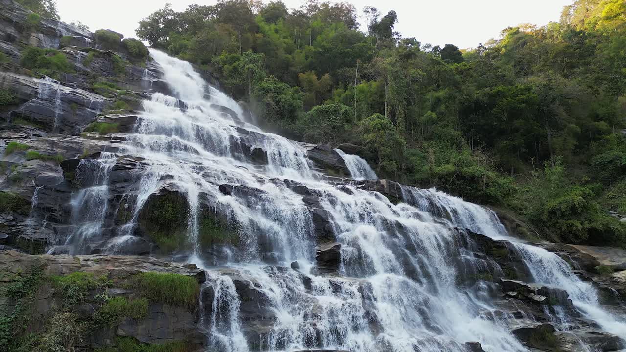 Aerial slowly ascends wispy Mae Ya waterfall in lush Thailand jungle