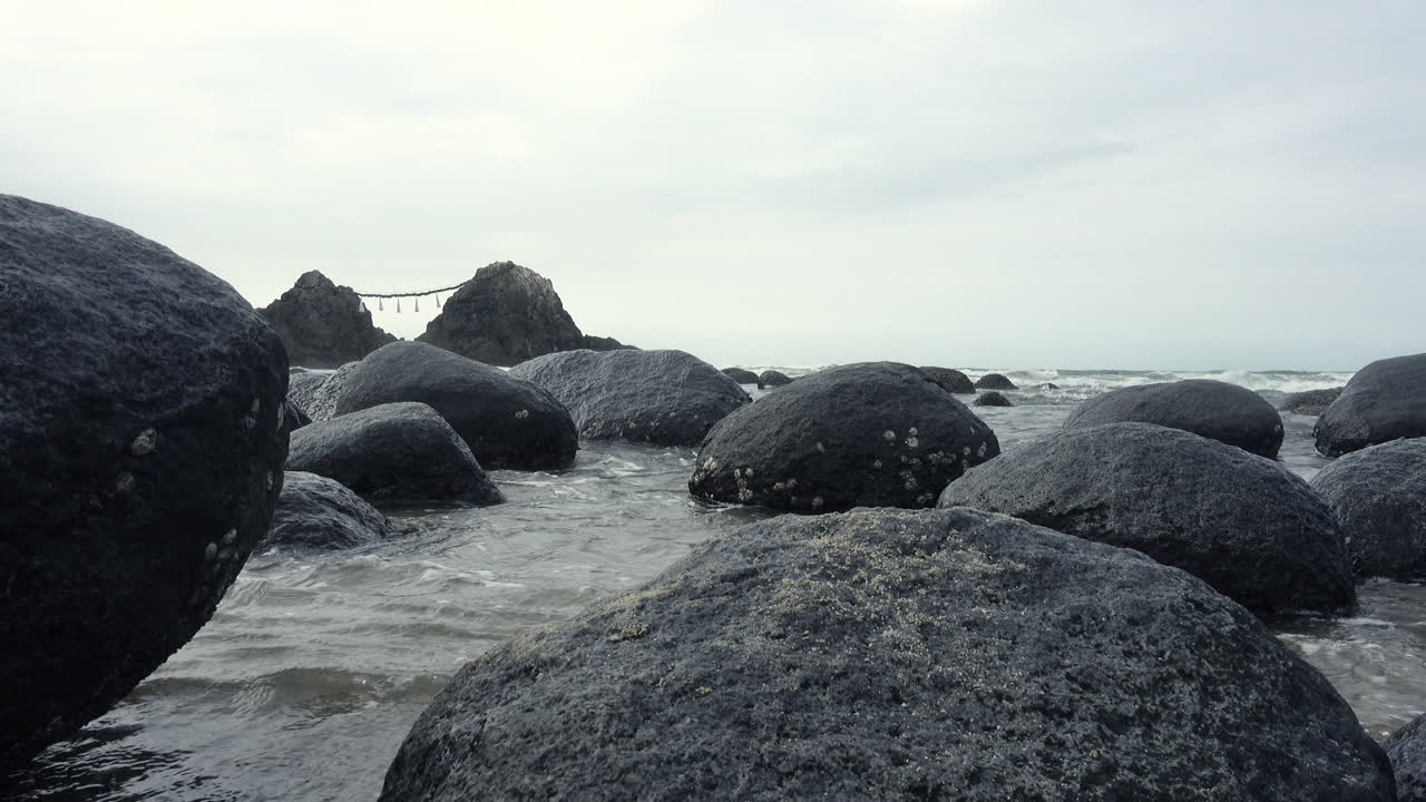 Sea   water getting between rocks reaching the sand on the shore of a beach with the ocean and a mountain background close up shot in 4K