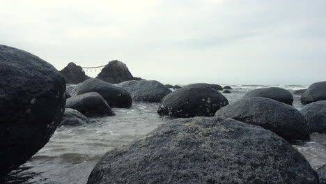 sea   water getting between rocks reaching the sand on the shore of a beach with the ocean and a mountain background close up shot in 4k