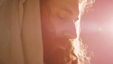 retroiluminado de cerca de un hombre vestido con túnicas con cabello largo y barba que representa la figura de jesucristo orando