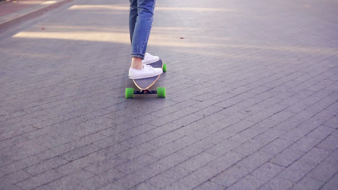 Close Up view of woman's legs in blue jeans and white sneakers skateboarding in the cobblestone road in the city. Legs on the