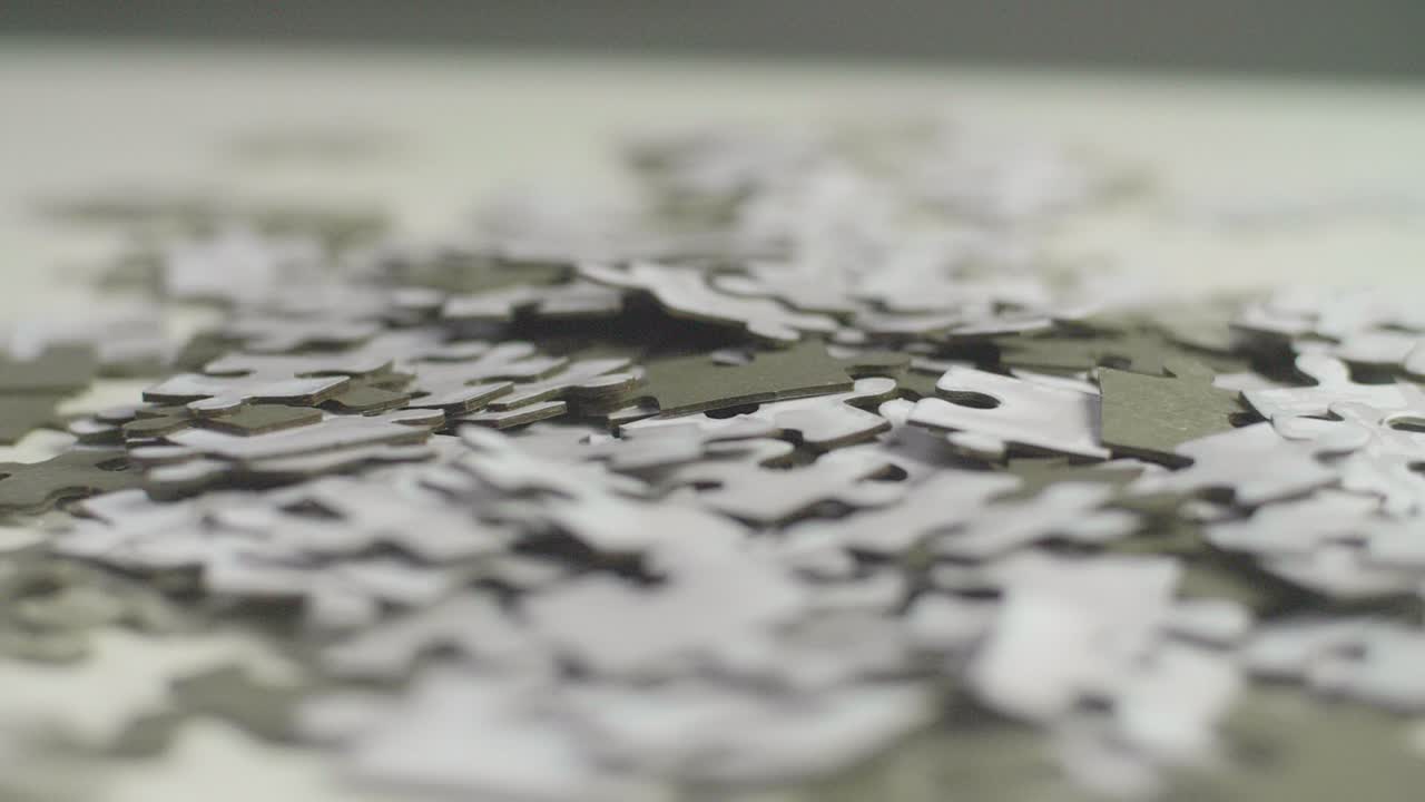 piezas de rompecabezas blancas y grises colocadas al azar sobre una superficie blanca girando lentamente con un fondo oscuro