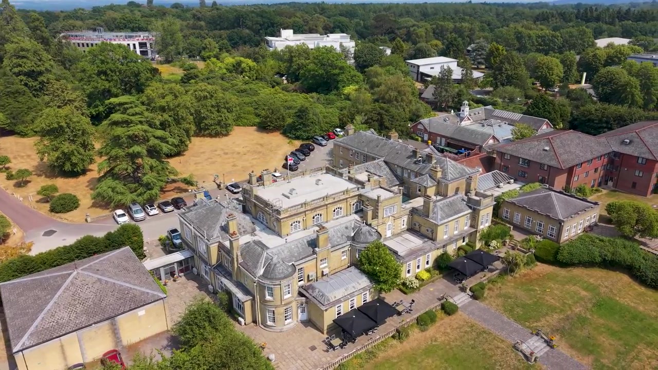 Drone kredser mod venstre omkring Chilworth Manor i Hampshire, England, og afslører parkeringspladsen, haverne og de skovklædte områder bag det historiske hus.