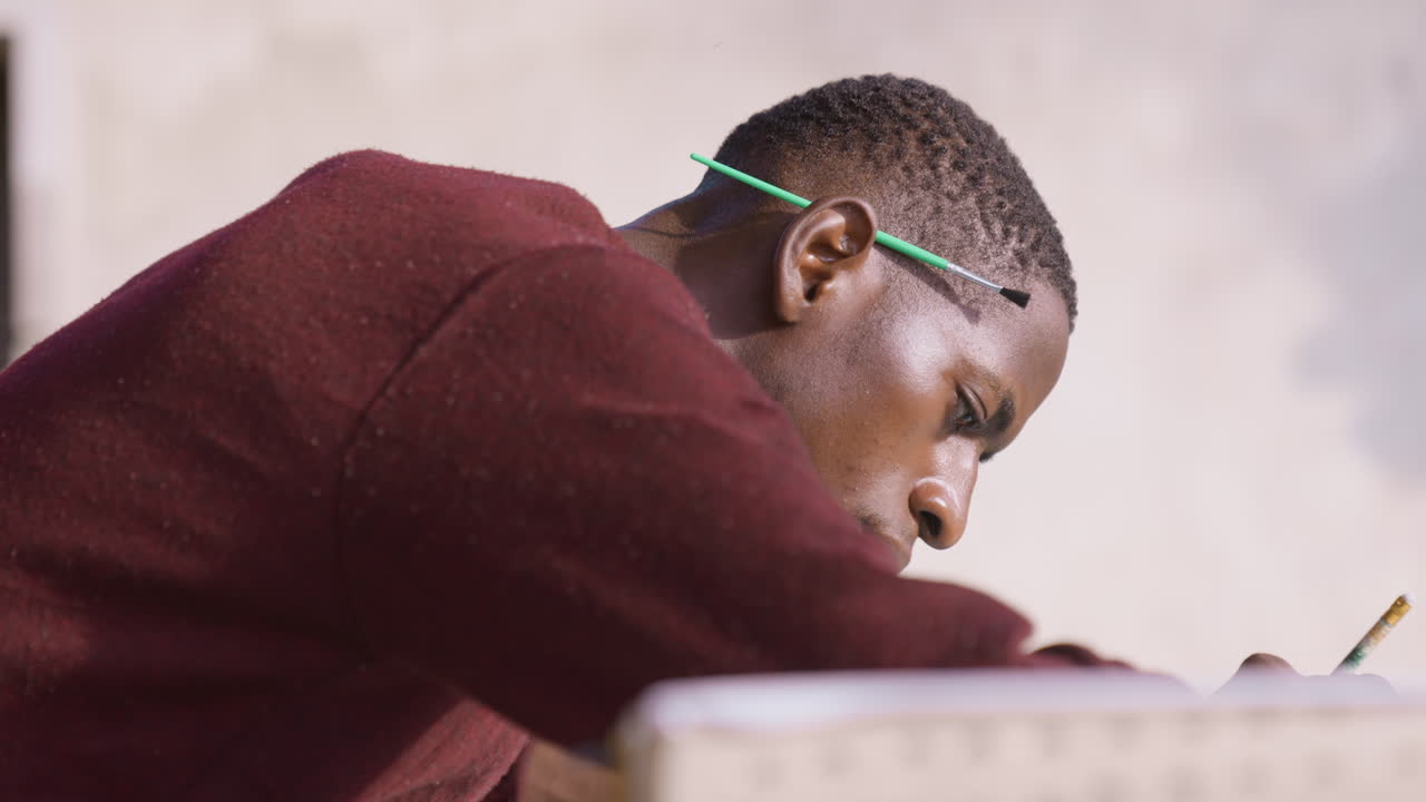 Black man executing fine brushwork on surface, intense closeup profile, pencil tucked behind ear, studio light catching textured pigment, steady hand guiding precise strokes, focused emotional