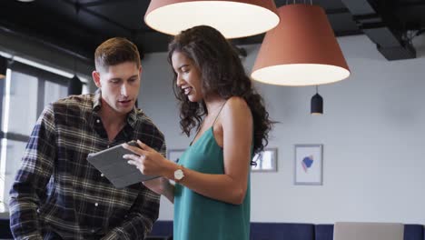 diverse male and female colleagues in discussion using tablet in casual office meeting, slow motion